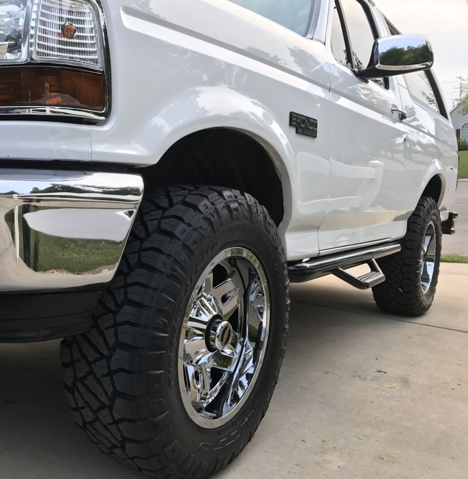 White 1995 Ford Bronco front quarter view, showing chrome wheels and side steps