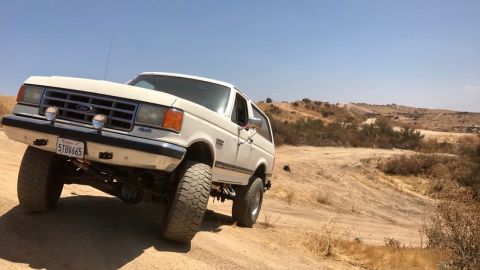 1988 Ford Bronco - This 1988 Ford Bronco navigates a dusty, off-road path under a clear blue sky.
