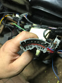 1988 Ford Bronco - A hand holds a complex wiring harness connector, revealing numerous exposed wires and connections within a vehicle's interior.