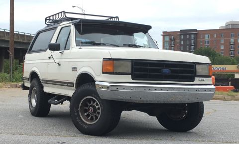 1988 Ford Bronco - This white 1988 Ford Bronco features a roof rack and is shown from a 3/4 front angle.