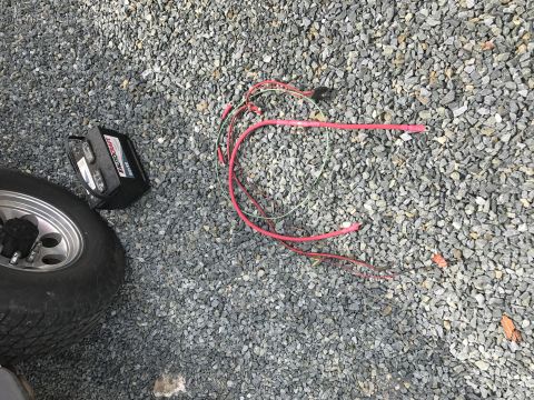 1992 Ford Bronco - A car battery and disconnected wiring lie on a gravel surface next to a tire.