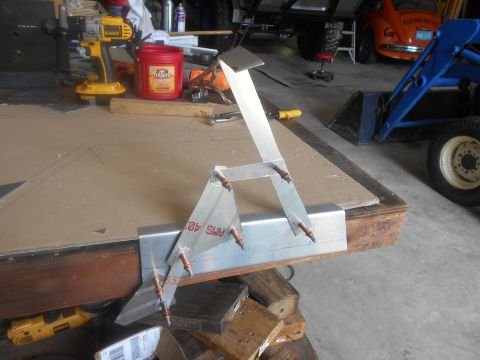 1992 Ford Bronco - A metal bracket assembly is on a workbench, with a blue tractor and an orange Volkswagen Beetle visible in the background.