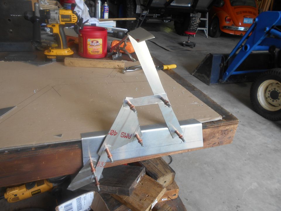 Metal bracket assembly on a workbench with tools and vehicles in the background