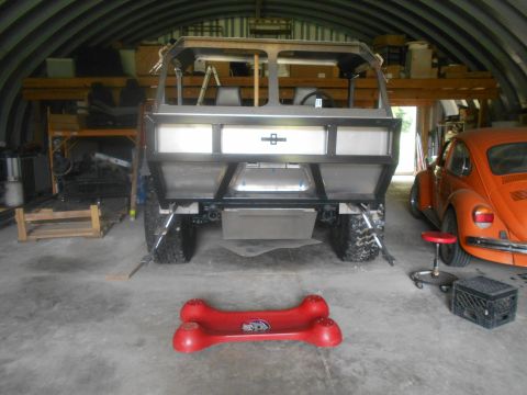 1992 Ford Bronco - Custom off-road vehicle chassis is in a garage next to an orange VW Beetle.
