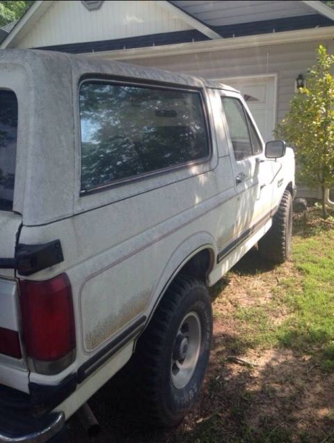 1988 Ford Bronco - This Ford Bronco is parked in a driveway next to a house and some trees.