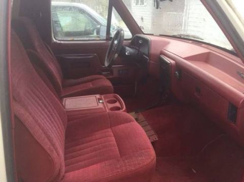 1988 Ford Bronco - Interior view of an older SUV with red velour seats and dashboard, showing the center console and steering wheel.