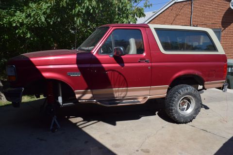 1995 Ford Bronco - This red Ford Bronco SUV, likely from the early to mid-1990s, is shown on jack stands with its front suspension exposed.