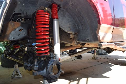 1995 Ford Bronco - Close-up of the front suspension of a 1995 Ford Bronco, showing red coil springs and a silver shock absorber.