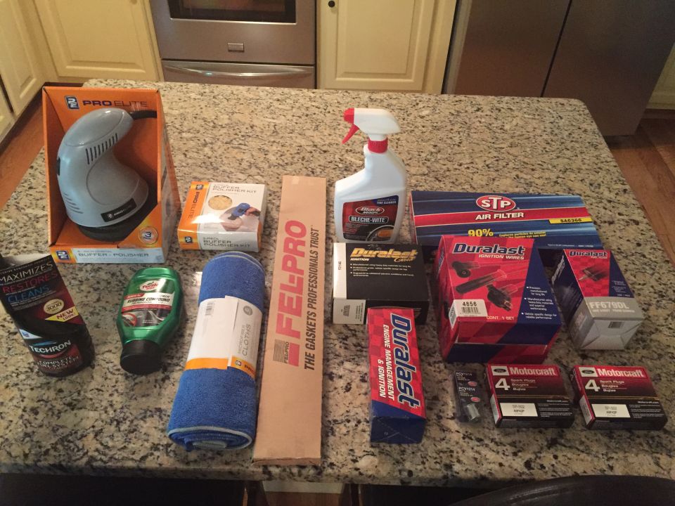 Car cleaning supplies, air filter, spark plugs, and buffer polisher laid out on a counter