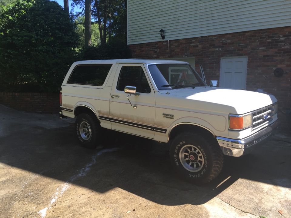 White Ford Bronco parked in driveway, driver's side visible, front quarter view
