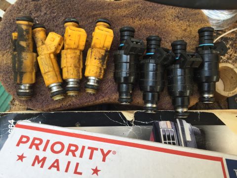 1988 Ford Bronco - A collection of used fuel injectors, some yellow and some black, are laid out on a textured surface.
