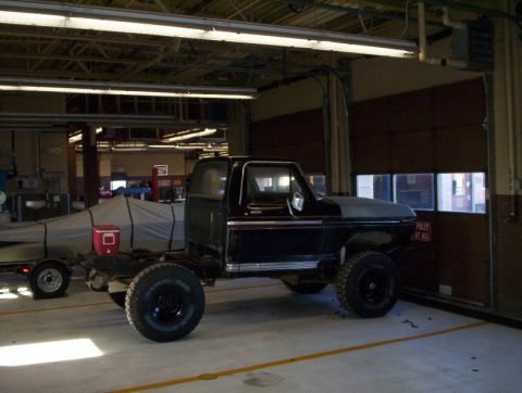 1978 Ford Bronco - A black truck chassis sits in a garage next to a boat covered by a tarp.