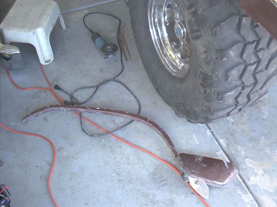 Stripped brown fender arch trim on garage floor beside angle grinder and mud-terrain tire