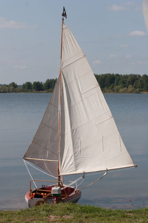 1993 Ford Bronco - A sailboat with white sails and a black flag is docked on a grassy shore next to a body of water.