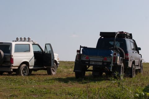 1993 Ford Bronco - Two off-road vehicles are parked on a grassy field under a clear blue sky. The vehicle on the left is a white SUV with its driver's door op…
