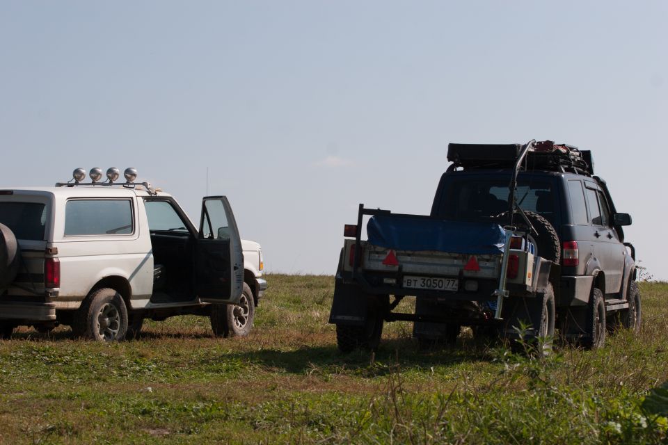 White and dark SUVs parked on a grassy field, one with its door open.