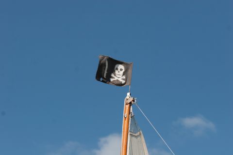 1993 Ford Bronco - A pirate flag with a skull and crossbones is flying from the mast of a sailboat against a clear blue sky.