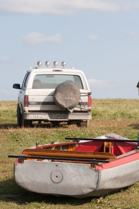 1993 Ford Bronco - The rear of a white Ford Bronco is parked on a grassy field with a spare tire mounted on the back. A red and gray boat is in the foreground.