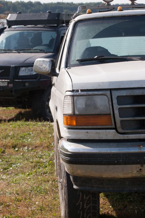 1993 Ford Bronco - The front-left side of a white 1990s Ford truck is shown parked on a grassy area, with a dark SUV visible behind it.