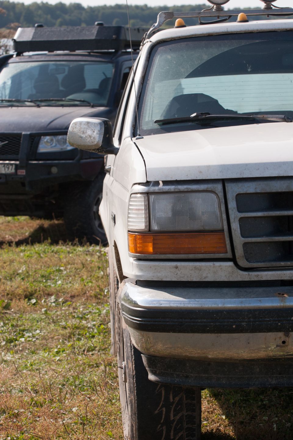 Front-left view of a white 1990s Ford truck with a black SUV behind it.