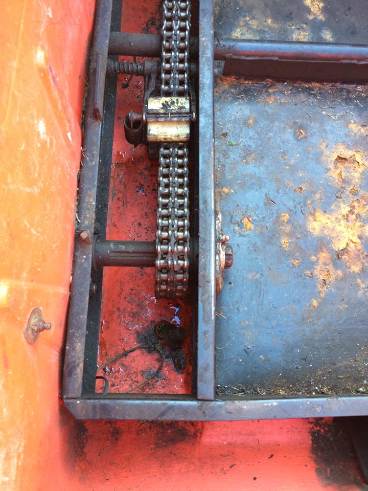 Close-up of a rusty chain and sprocket on an orange and blue vehicle.