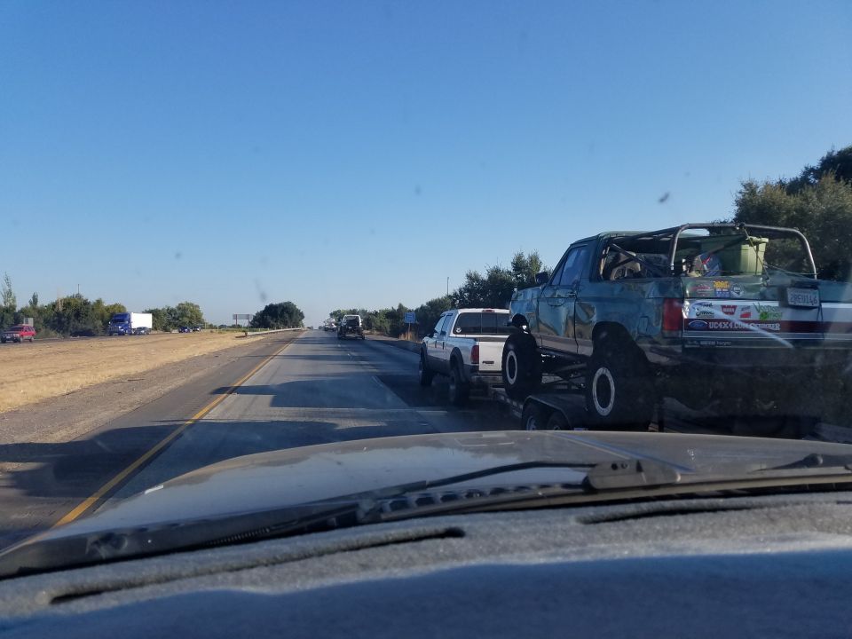 Modified teal Ford Bronco on a trailer on a highway, with a roll cage and off-road tires.