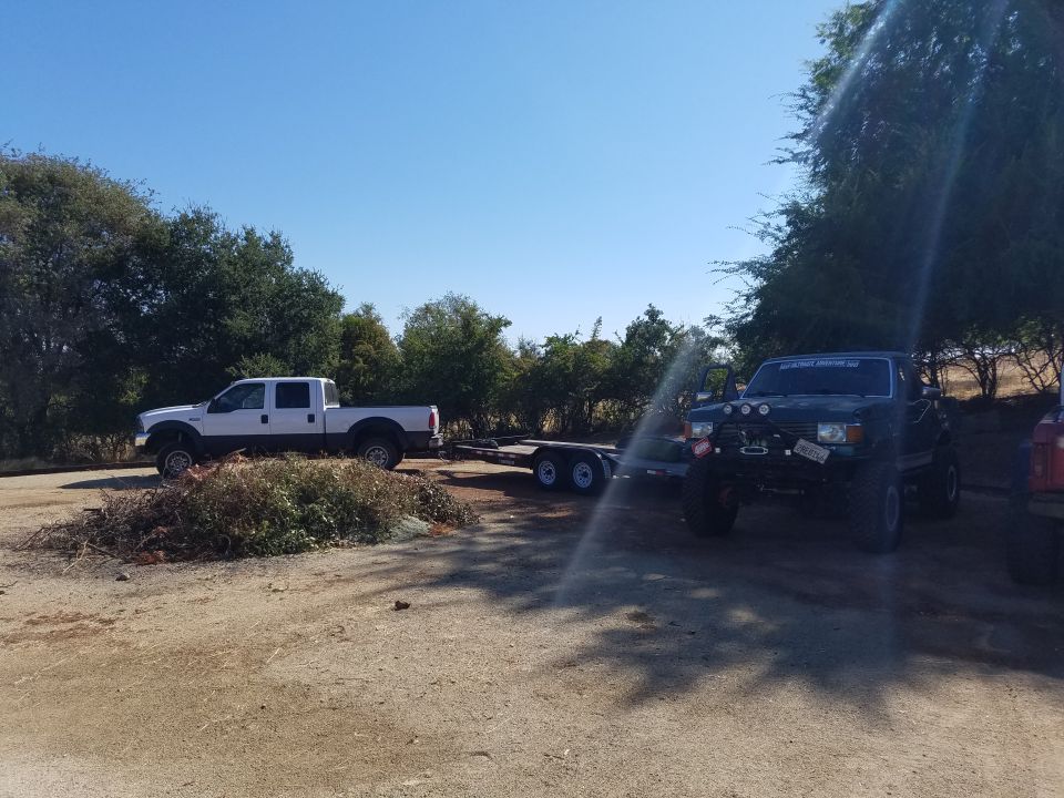 Lifted dark SUV with off-road lights and winch parked on dirt lot next to brush pile.