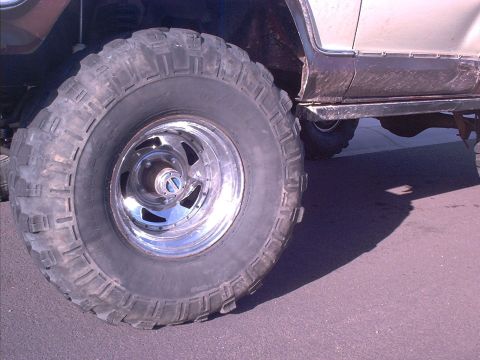 1979 Ford Bronco - A close-up view focuses on the aggressive tread of a large off-road tire mounted on a shiny chrome wheel.