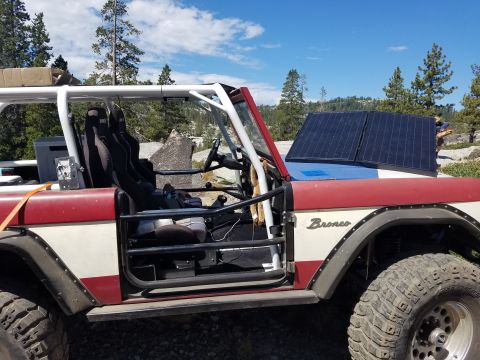 1968 Ford Bronco - The side view of a red and white 1968 Ford Bronco shows its interior with racing seats and a roll cage. Two solar panels are mounted on the…