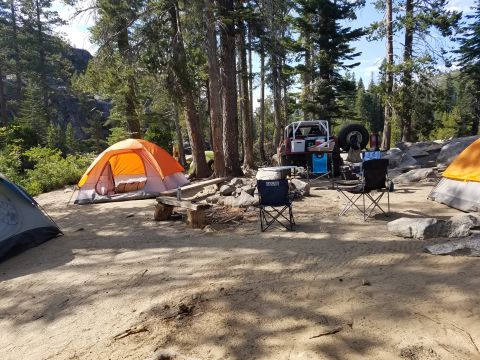 1968 Ford Bronco - A campsite scene features an orange and gray tent set up on sandy ground, with a red off-road vehicle parked in the background. Several cam…