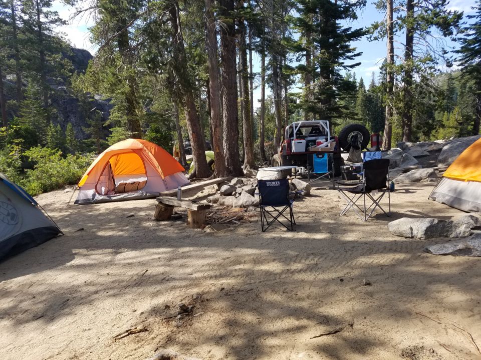 Orange and gray tent with a red off-road vehicle and camping chairs at a campsite.