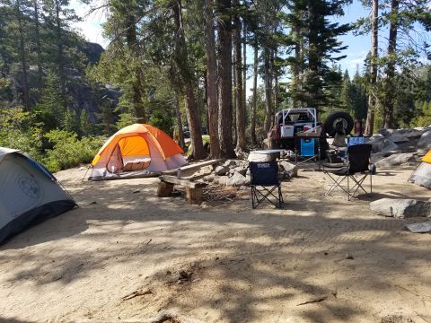 1968 Ford Bronco - A campsite scene features an orange and gray tent, a silver and gray tent, several camping chairs, and a red off-road vehicle with a spare…