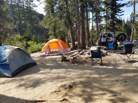 1968 Ford Bronco - A red off-road vehicle with a spare tire mounted on the back is parked at a campsite with two tents and camping chairs.
