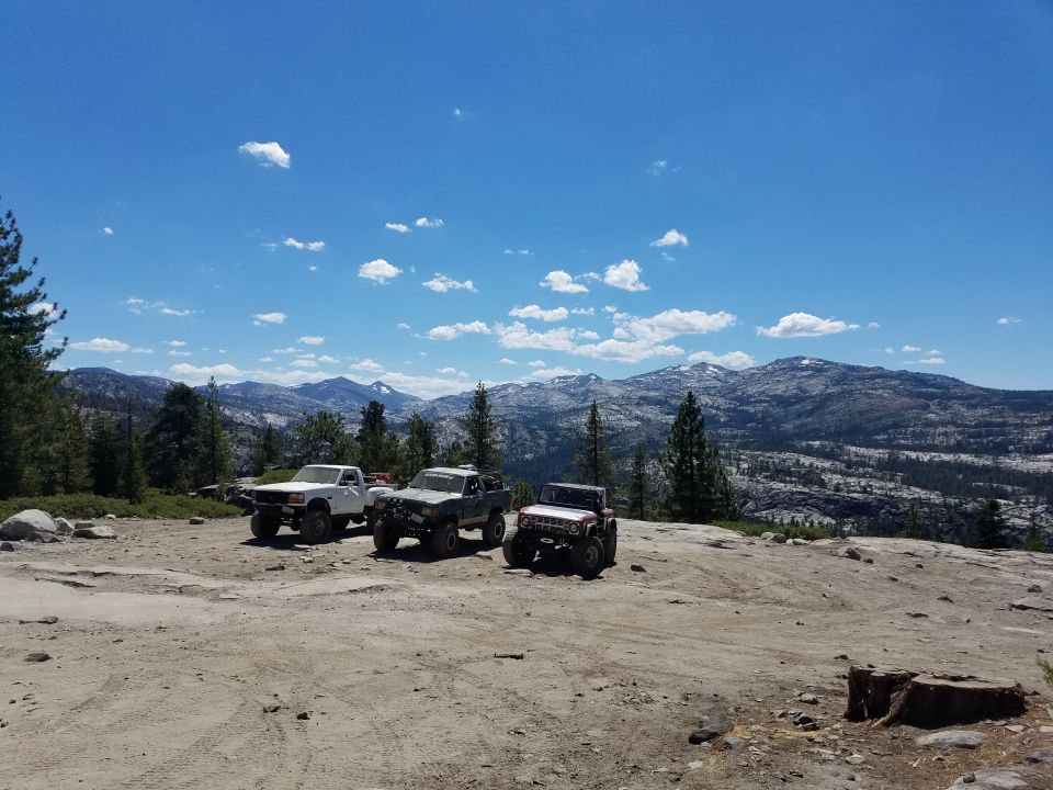 Three off-road vehicles parked on a rocky clearing with mountains in the background.
