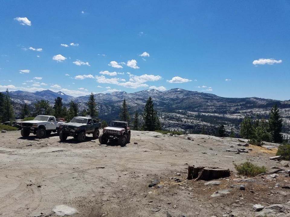 Three modified off-road vehicles parked on a rocky clearing with mountains in the background.