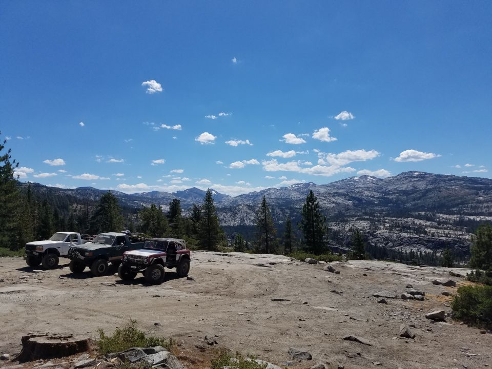 Three off-road vehicles parked on a rocky clearing with mountains in the background.