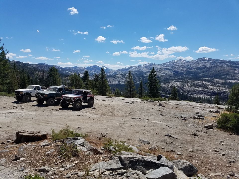 Three off-road vehicles parked on a rocky plateau with mountains in the background.