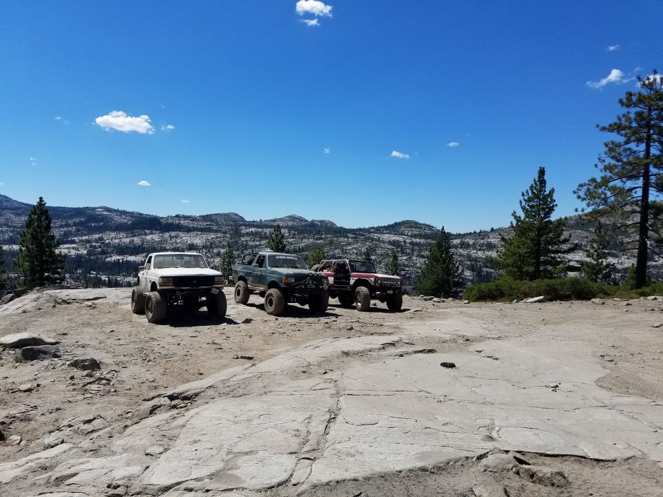 Four modified off-road trucks parked on a rocky, mountainous landscape.