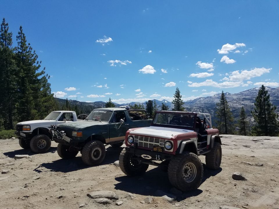 Three off-road trucks and SUVs parked on a rocky surface with mountains in the background.