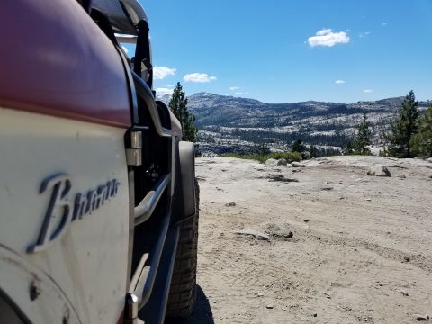 1968 Ford Bronco - A side view of a vintage red and white Ford Bronco parked on a rocky, dusty terrain with a mountainous landscape in the background under a…