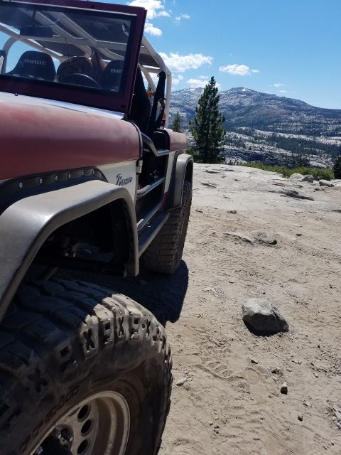 1968 Ford Bronco - A close-up, low-angle side view of a red and white Ford Bronco parked on a dirt and rock-covered overlook with a mountain range in the back…
