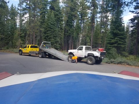 1968 Ford Bronco - A white Ford pickup truck with large tires is being worked on by a person in an orange shirt next to a yellow tow truck with its bed extend…