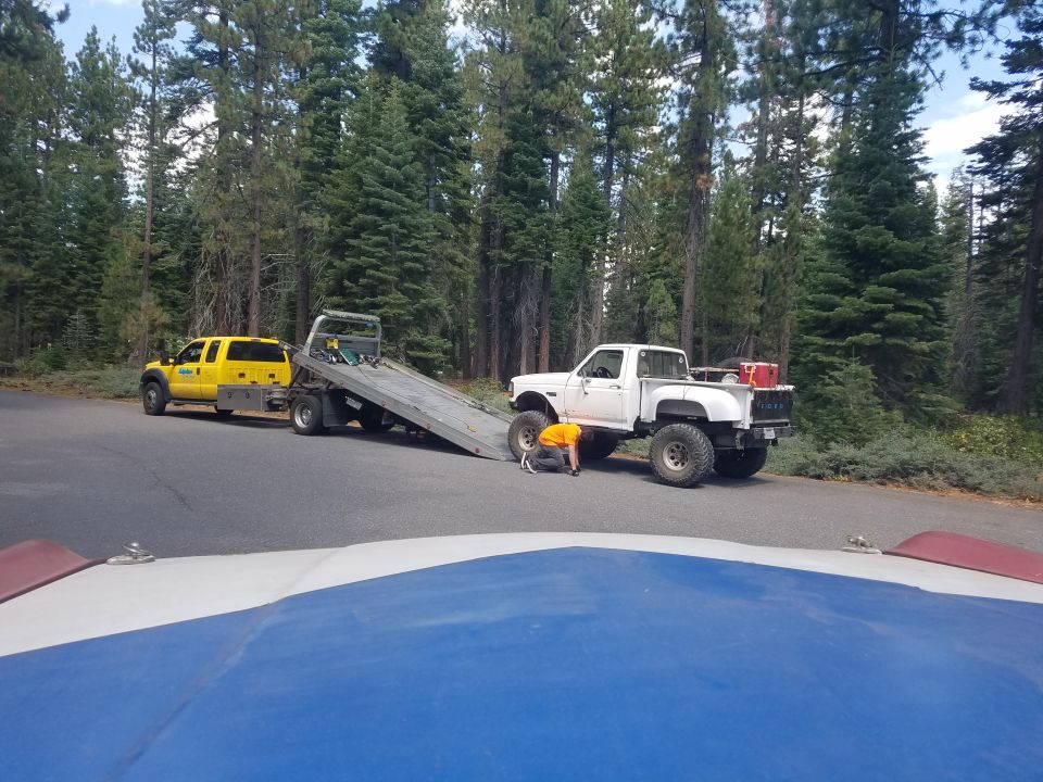 White Ford pickup truck with large tires being serviced next to a yellow tow truck.