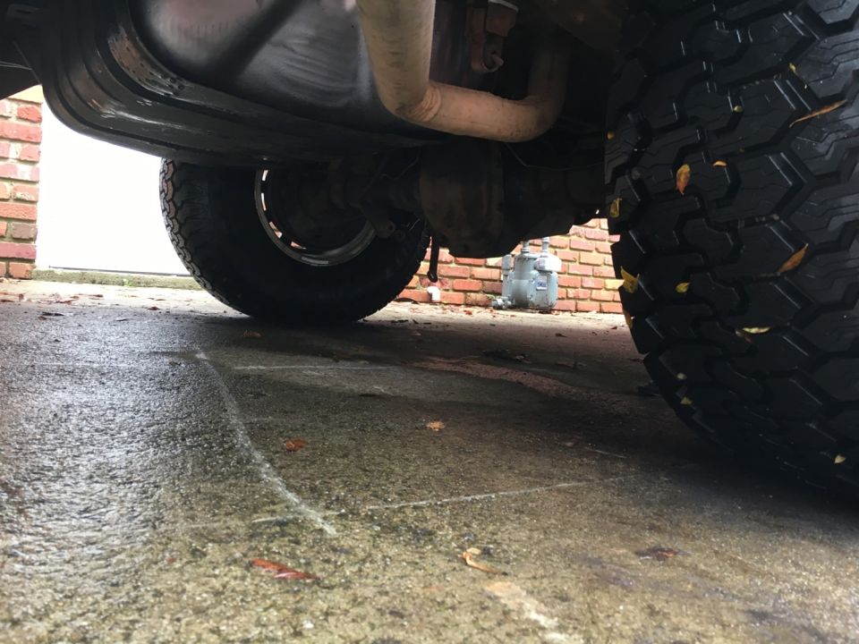 Underside of a vehicle showing rear tire, exhaust, and differential on a wet driveway.