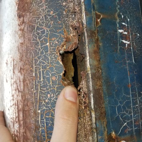 1967 Ford Bronco - Close-up of significant rust damage and peeling paint on a vehicle part.