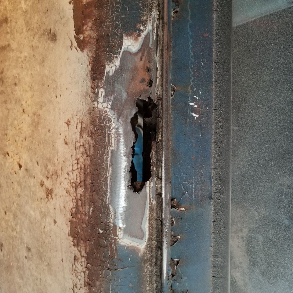 Close-up of rusted and holed blue vehicle body panel.
