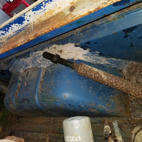 1967 Ford Bronco - A close-up view of a rusty metal component, possibly a driveshaft, resting on a blue painted surface with peeling paint and rust. A white f…