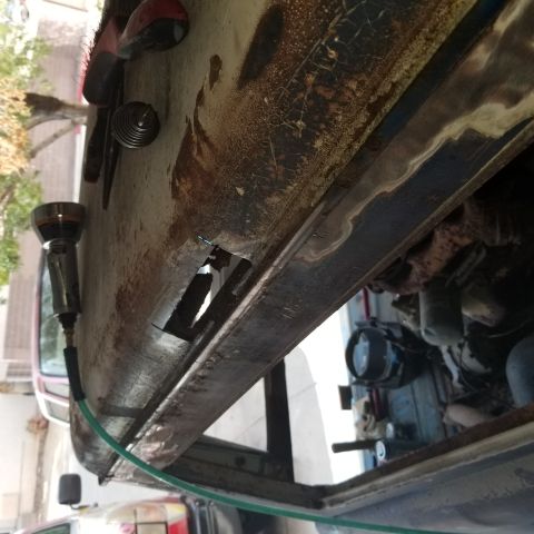 1967 Ford Bronco - A close-up view of a heavily rusted vehicle door with a rectangular hole cut into it. A pneumatic tool with a green hose is attached to the…