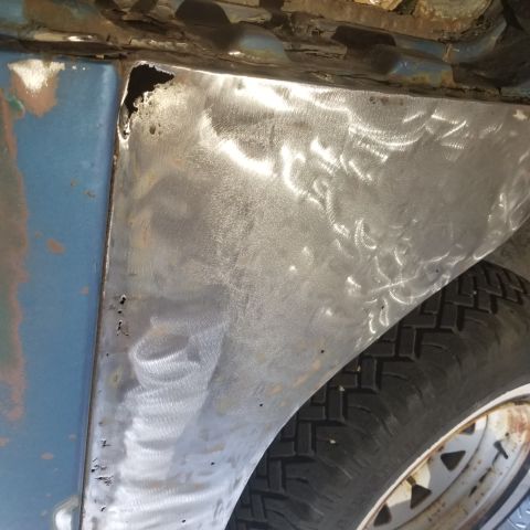 1967 Ford Bronco - A close-up view of a metal patch on the fender of a blue vehicle, showing evidence of recent bodywork and some rust.