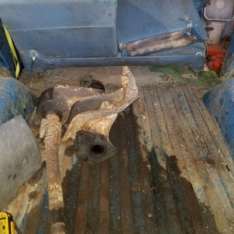 1967 Ford Bronco - A rusty driveshaft and differential assembly is lying on the floor of a blue vehicle's cargo area, next to a worn blue bench seat.
